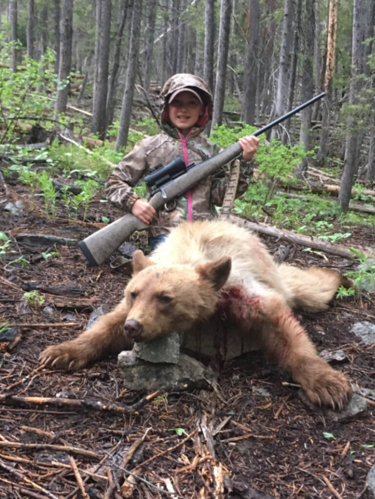 A small boy holding a gun with a dead deer