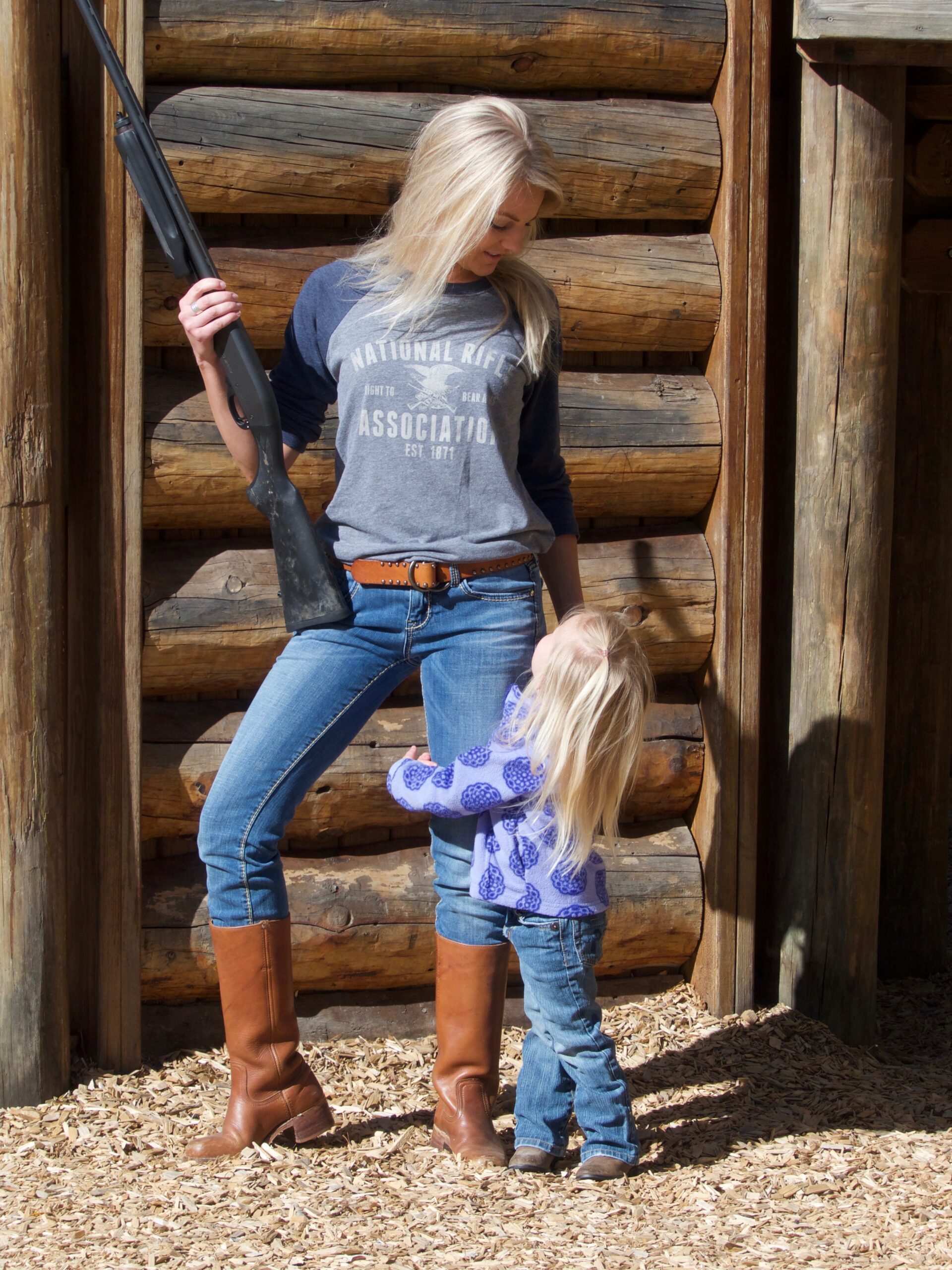 A girl standing with a small child holding a gun